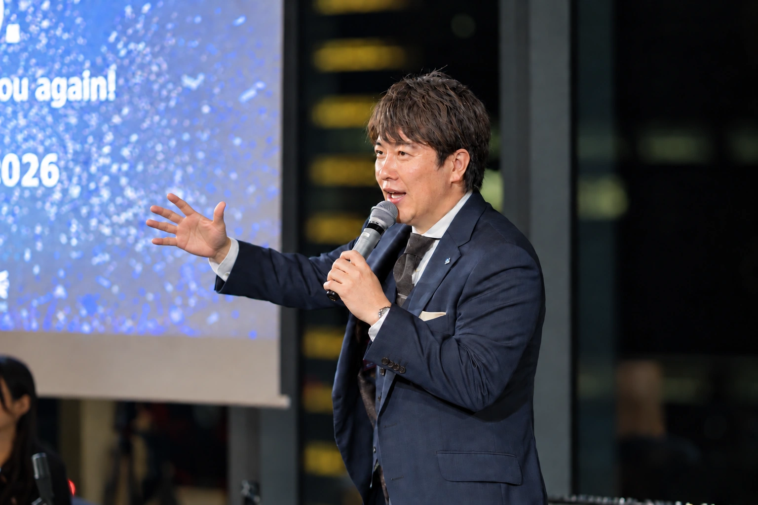 新年会2026で、マイクを手に参加者へ語りかける様子